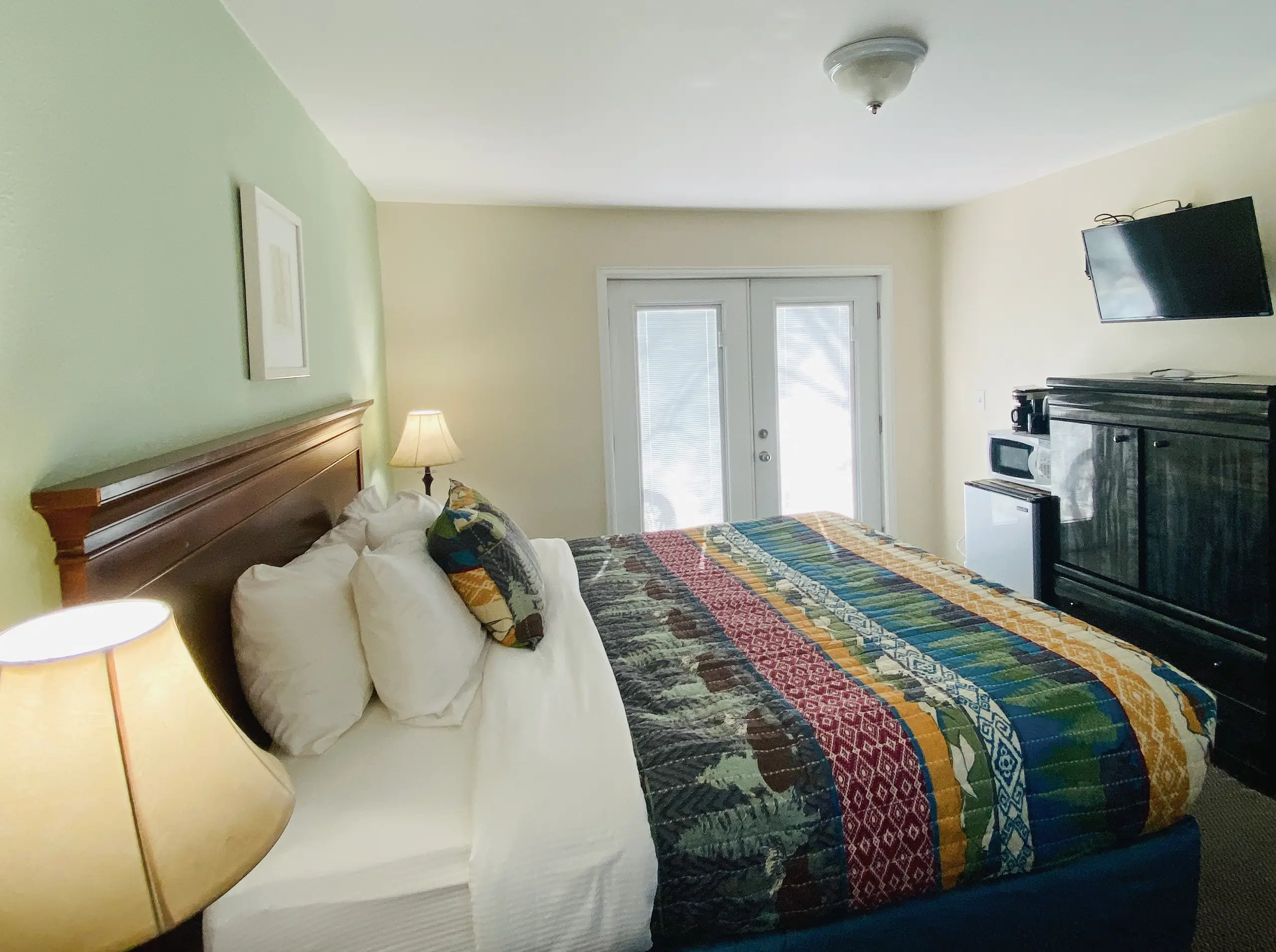 King bed with patterned quilt and tv on wall